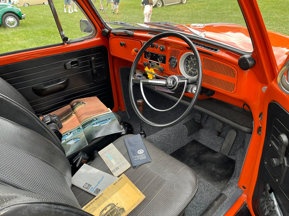 Orange VW Super Beetle interior with vintage manuals and camera on seat at outdoor show