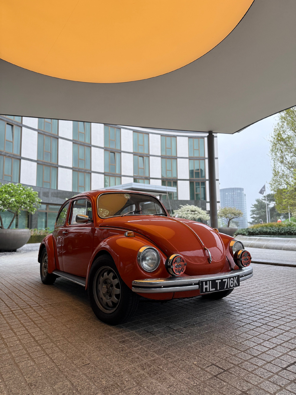 Orange VW Super Beetle parked under circular light canopy with chrome bumpers and fog lights