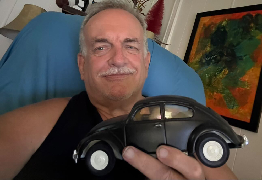 Jim holding a small black VW Beetle model in front of colorful artwork