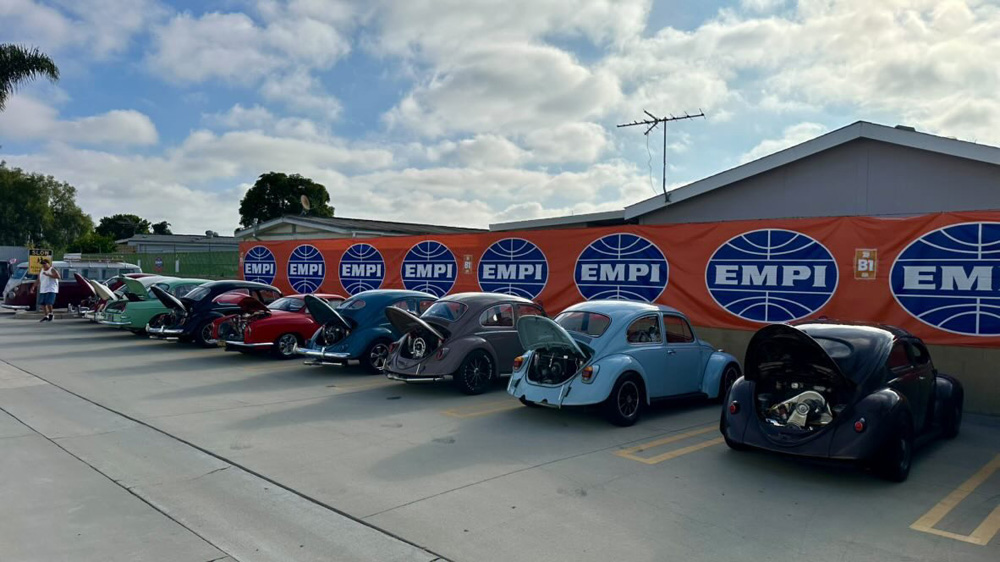 Row of classic Volkswagen Beetles with open engines in front of an EMPI banner at the EMPI 70th Anniversary Open House