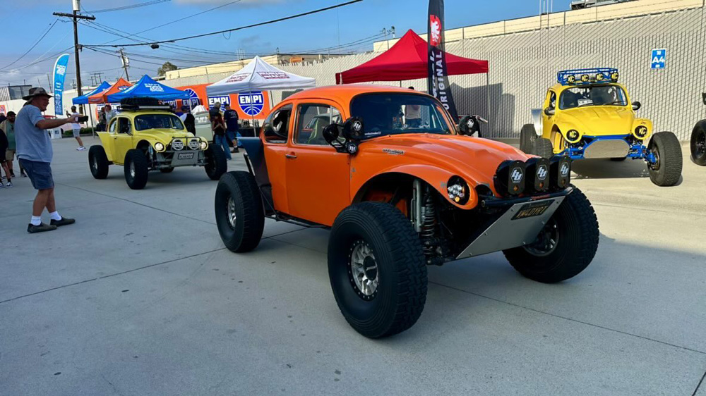 Lineup of orange and yellow Baja Bugs with off road lights parked near EMPI tents at the EMPI 70th Anniversary Open House