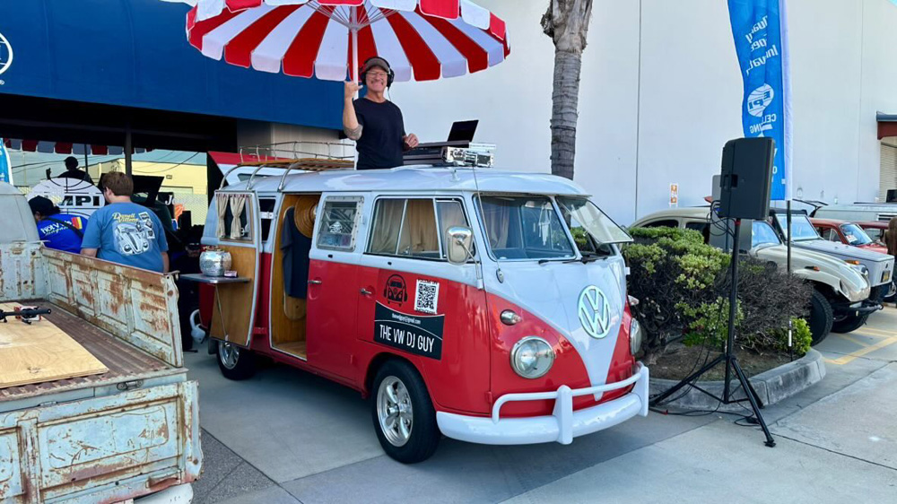 Red and white Volkswagen Bus converted into a DJ booth with a striped umbrella at the EMPI 70th Anniversary Open House