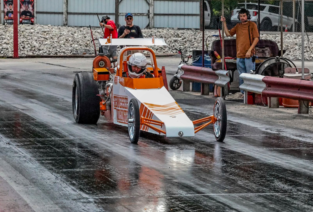 White and orange dragster at the starting line with crew standing nearby